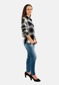 Camisa de cuadros en blanco y negro con mangas largas, combinada con jeans azules. La figura lleva unos zapatos de tacón altos negros.