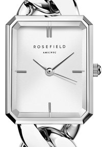 Reloj rectangular plateado con un dial blanco estriado, bisel octagonal y delgadas manecillas de hora y minuto. Sujeto a una robusta correa de eslabones de cadena plateada.