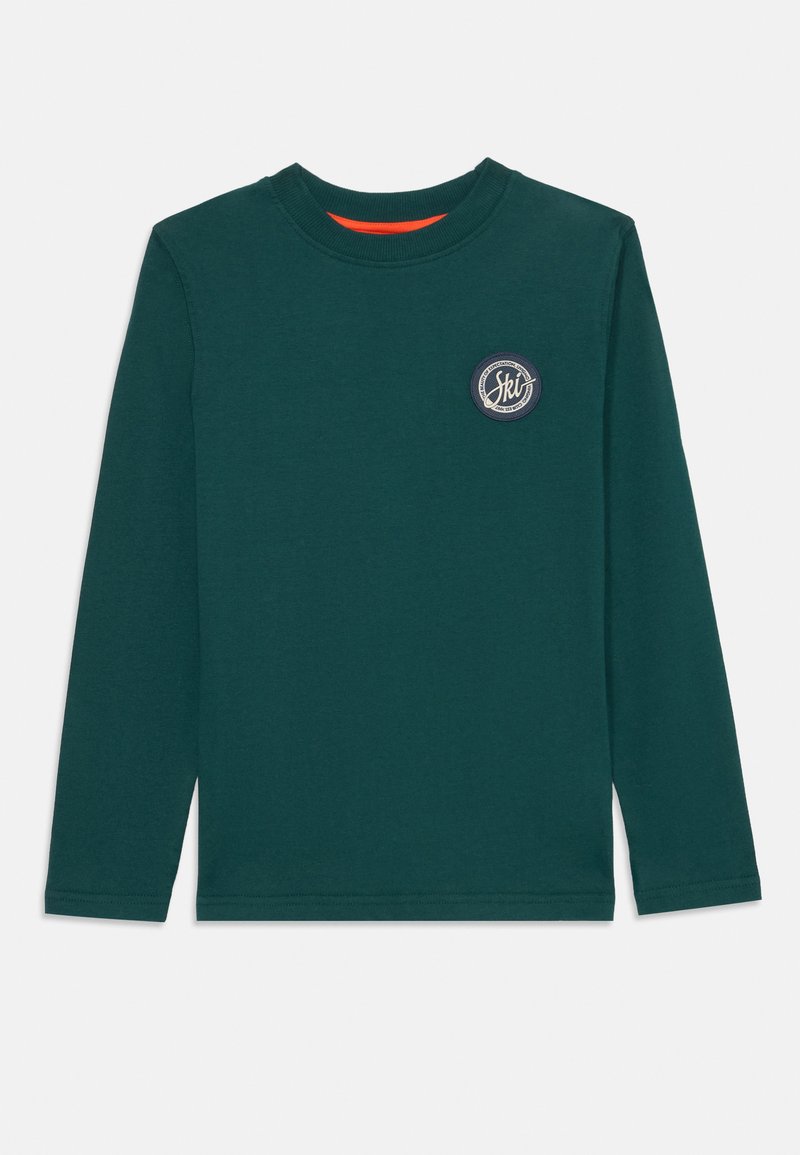 Hosszúujjú sötétzöld pamut póló, kerek nyakkivágással, a mellkason kör alakú sílogóval és narancssárga részlettel a gallér belső oldalán.