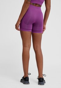 Shorts de sport en tricot violet avec une coupe ajustée, texture lisse et taille haute. Présente des coutures minimales et se marie avec des chaussures de sport noires.