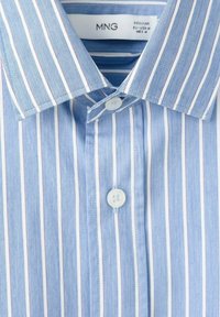 Modra in bela srajca s črtami, ki ima ovratnik s šilastimi konicami, sprednji del z gumbi, belimi gumbi in gladko teksturo.