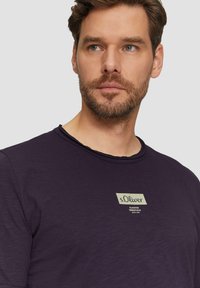 Lila Baumwoll-T-Shirt mit Rundhalsausschnitt und strukturiertem Finish. Verfügt über ein rechteckiges Markenlabel in hellem Beige auf der Brust.