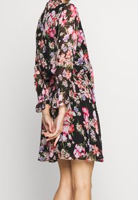 Kwiatowa sukienka z czarnym tłem i różowymi oraz fioletowymi kwiatami, z długimi rękawami ozdobionymi falbanami i dopasowanym stanem.