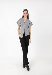 Top corto gris de manga corta con escote en V, abrochado con un botón plateado, combinado con pantalones acampanados negros y botas negras de punta.