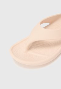 Svetloružové šľapky s textúrovanou stielkou, T-popruhom a hladkým povrchom. Vyrobené z flexibilného materiálu pre pohodlie.