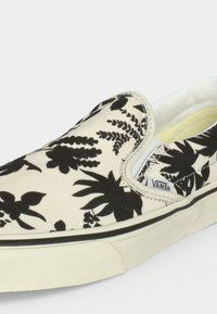 Slip-on παπούτσι Vans με μαύρο λουλουδάτο μοτίβο σε λευκό φόντο και λευκή λαστιχένια σόλα με μαύρη ρίγα.