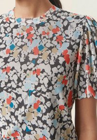 Blommig kortärmad topp med svart bakgrund, prydd med färgglada mönster i röd, blå och beige. Mjuk tygkvalitet med rund halsringning.