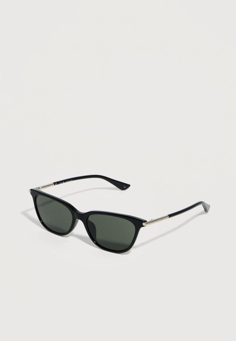 Μαύρα ορθογώνια γυαλιά ηλίου με σκοτεινούς φακούς και λεπτές ασημένιες λεπτομέρειες στα πλαϊνά, τοποθετημένα σε ανοιχτή επιφάνεια.