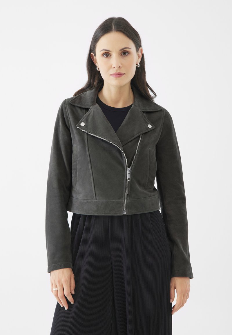 Chaqueta de motocicleta de ante gris oscuro, recortada, con cremallera plateada, cuello de solapa y dos bolsillos frontales. Llevada sobre una blusa negra.