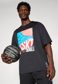 Melna īsām piedurknēm T-kreklu ar krāsainu kvadrātveida grafiku, kas attēlo basketbola motīvus; valkāts kopā ar teksturētu melnu basketbola bumbu.