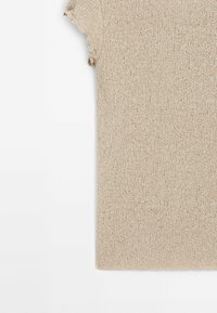 Pull beige en maille à manches courtes avec un motif texturé et des bords à volants aux manches.