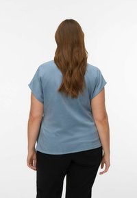 Haut bleu clair à manches courtes avec une texture lisse, un col arrondi et une coupe décontractée, associé à un pantalon noir. Vue de dos.