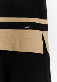 Tessuto lavorato a maglia nero e beige con strisce orizzontali, dotato di uno spacco laterale e di un piccolo logo metallico per dettagli.