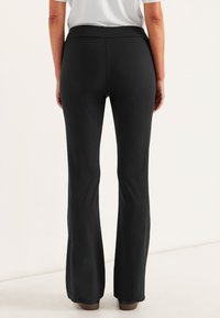 Zwarte flared broek met een brede tailleband, gemaakt van rekbaar materiaal. Gladde textuur, geen zichtbare patronen, en een zoom die de schoenen aanraakt.