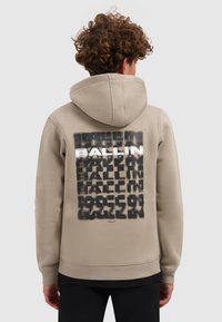 Beige hoodie met een grote grafische print op de achterkant, voorzien van zwart-wit tekstontwerp. Zachte textuur, kangoeroezak en capuchon.