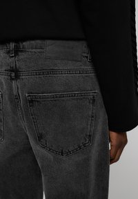 Black denim jeans with a slightly faded texture, featuring two back pockets and a black leather patch labeled "Eightyfive."