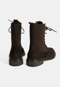 Bruine suède enkellaarsjes met een ribbelstofsectie, vetersluiting aan de voorkant en een stevige zwarte rubberen zool. Voorzien van een trekband voor eenvoudig aan- en uittrekken.