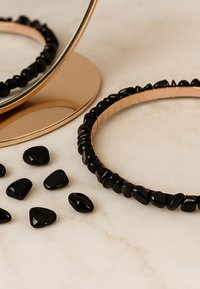 Naszyjnik z czarnych kamiennych koralików w okrągłym wzorze, z gładkimi, błyszczącymi koralikami; prezentowany z luźnymi, pasującymi kamieniami na marmurowej powierzchni.