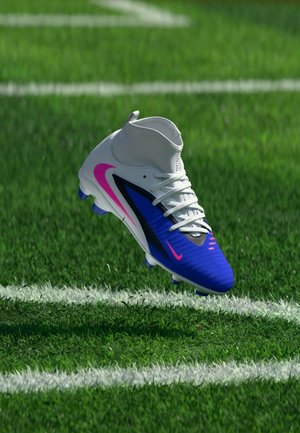 Hvid og blå fodboldstøvle med pink accenter svævende over grøn græs nær en hvid linje på banen.