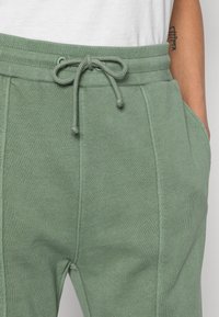 Pantalones de chándal de color verde claro con cintura ajustable, bolsillos laterales y puños acanalados. Fabricados en un material suave y texturizado.