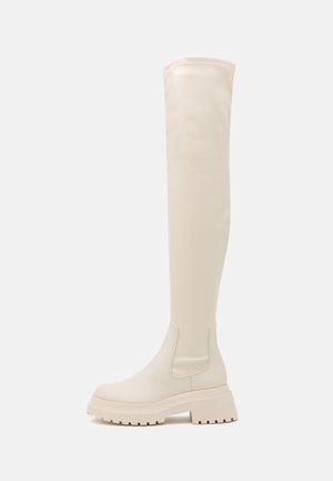 Bílé kozačky do výše kolen vyrobené z hladkého syntetického materiálu, s robustní podrážkou a minimalistickým designem s elegantními liniemi.