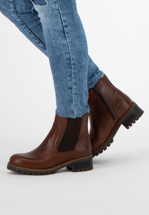 Hnědé kožené kotníkové boty s elastickými bočními panely, kulatou špičkou a robustní gumovou podrážkou. Nesené s světle modrými džíny.