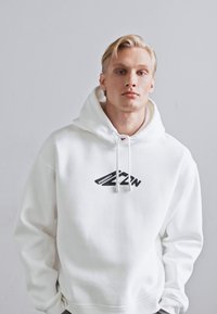 Sudadera blanca con cordón, que presenta un logo negro en el pecho. Fabricada en una tela suave, tiene un ajuste holgado y cómodo.