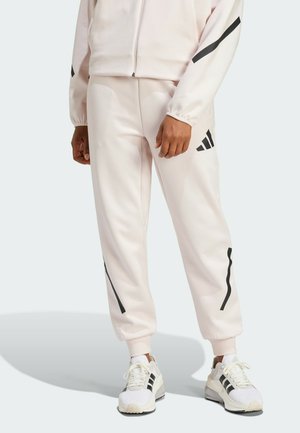 Pantalones jogger de color rosa claro con rayas diagonales negras, cintura elástica y puños acanalados, combinados con zapatillas blancas con acentos negros.