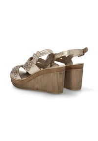 Sandalias de cuña beige con una plataforma texturizada, diseño floral recortado en la parte delantera, correa ajustable en el tobillo y acentos metálicos.