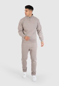 Lichtbruine zip-up sweatshirt en bijpassende joggers van zacht materiaal, met zakken en geribbelde manchetten. Draag met witte sneakers.