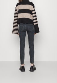 Besklippt svart och beige randig tröja med långa ärmar, kombinerad med mörka skinny jeans och kraftiga svarta skor.