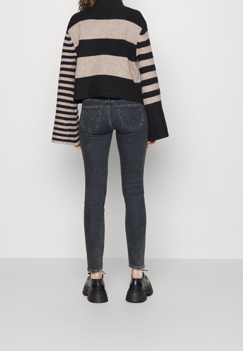 Besklippt svart och beige randig tröja med långa ärmar, kombinerad med mörka skinny jeans och kraftiga svarta skor.