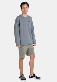 Gray long-sleeve shirt with black logo, paired with green shorts. Sneakers are black with white accents. Fabric appears soft and casual.