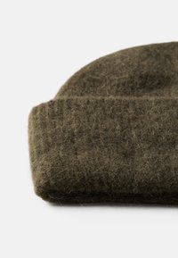 Grøn uld hue med et struktureret, strikket mønster. Har en foldet kant, der viser en blød, fuzzy overflade.