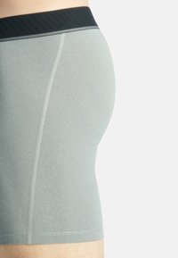 Grå boxershorts med svart ribbad midja. Tyget är glatt med en lätt glans och har platta sömmar för komfort.