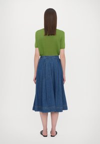 Maglione verde a maniche corte, abbinato a una gonna midi plissettata in denim blu. La gonna presenta un dettaglio di cucitura sull'orlo e una cintura.