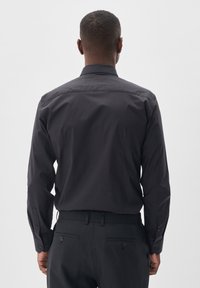 Camisa negra de manga larga con un cuello tradicional, puños abotonados y una textura suave. La parte trasera tiene un diseño limpio sin logotipos visibles.