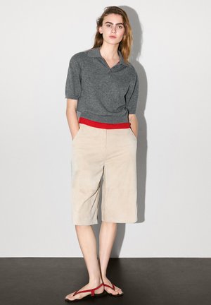 Gray short-sleeve polo shirt with a red waistband paired with beige culottes. Sandals with red straps. Simple, relaxed fit.