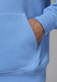 Sweat-shirt bleu clair avec une poche kangourou et des poignets côtelés, fabriqué en tissu doux à texture lisse avec des détails de couture contrastants.