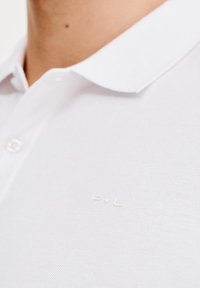Biała koszulka polo z teksturowanej tkaniny, z klasycznym kołnierzykiem i małym, wytłoczonym logo na piersi.