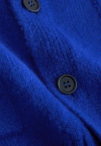 Diepblauwe wollen stof met een getextureerd oppervlak, met twee zwarte knopen langs een naad.