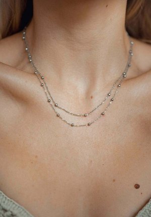 Collana doppia strato in argento con piccole perle sferiche, design a catena delicato, che poggia su una clavicola scoperta.