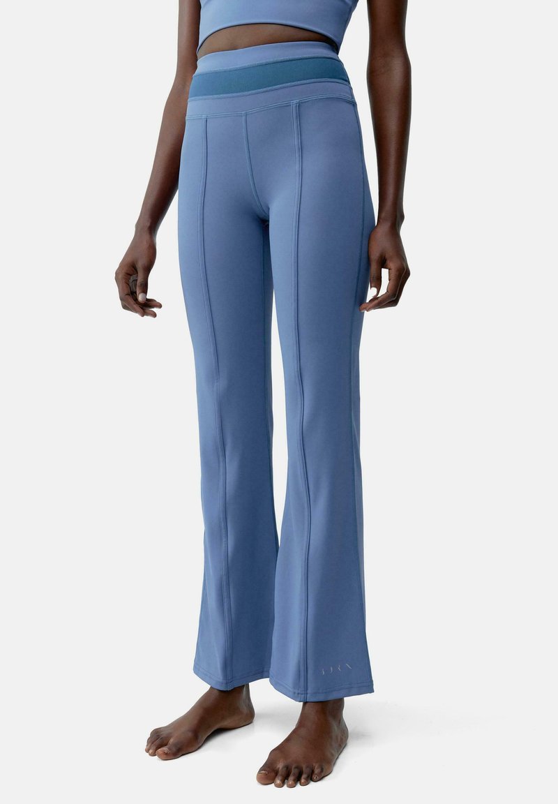 Pantaloni yoga svasati blu con vita alta, realizzati in tessuto elastico con cuciture piatte e una superficie liscia.