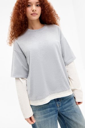 Gray short-sleeve t-shirt layered over a long-sleeve white shirt, featuring a relaxed fit and soft texture. Worn with blue jeans.
