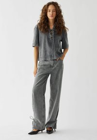 Outfit in denim grigio composto da una maglietta a maniche corte con dettagli in laccio e pantaloni a gamba larga con legacci regolabili all'orlo.