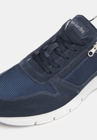 Scarpa atletica in suede e rete color navy con lacci e zip laterale, caratterizzata da una suola bianca e dettagli testurizzati sulla parte superiore.