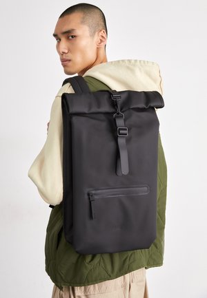 Black roll-top backpack made of textured, waterproof material; features a front zipper pocket and adjustable straps.