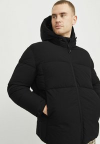 Must must jacket kõrge kaeluse ja kapuutsiga, millel on täispikk tõmblukk ja küljetaskud. Sile tekstuur mati viimistlusega.