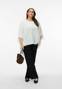 Biała, zwiewna tunika z szerokimi rękawami, zestawiona z czarnymi, luźnymi spodniami i brązową zamszową torbą typu bucket. Całość dopełniają ciemne buty.