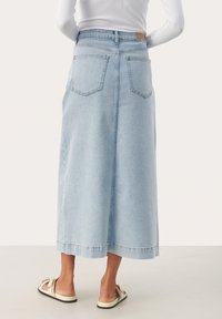 Jupe midi en denim bleu clair avec poches arrière, une silhouette droite et un ourlet brut. Associée à des tongs décontractées, mettant en valeur un design simple.